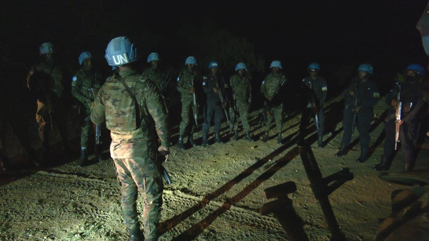 A group of peacekeepers standing together in a group with one peacekeeper leading the discussion. It is nighttime in the photo.