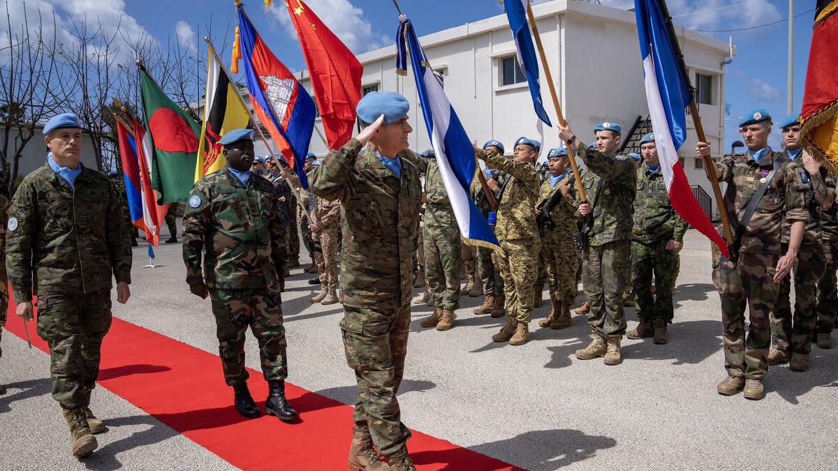 Peacekeepers hold flags as the Force Commander salutes.