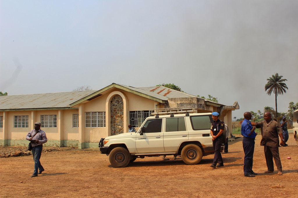 A few staff members standing by a car and a house on the field